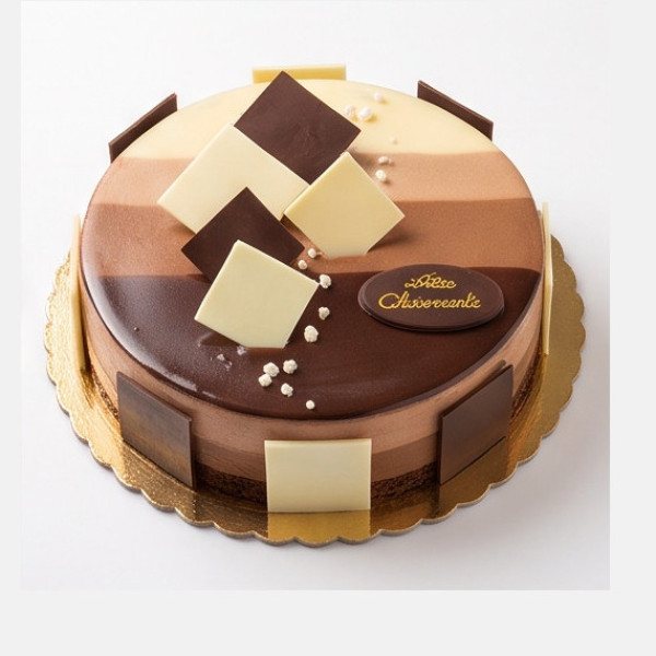 Torta rotonda a strati di cioccolato, con superficie a fasce chiare e scure e quadrati di cioccolato su un vassoio dorato.